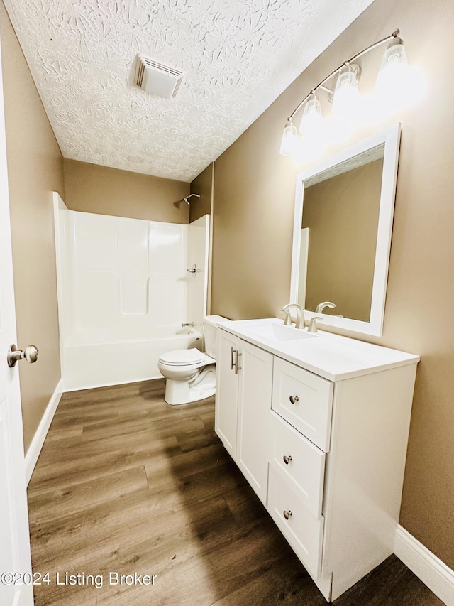 full bathroom with bathing tub / shower combination, a textured ceiling, toilet, vanity, and hardwood / wood-style flooring