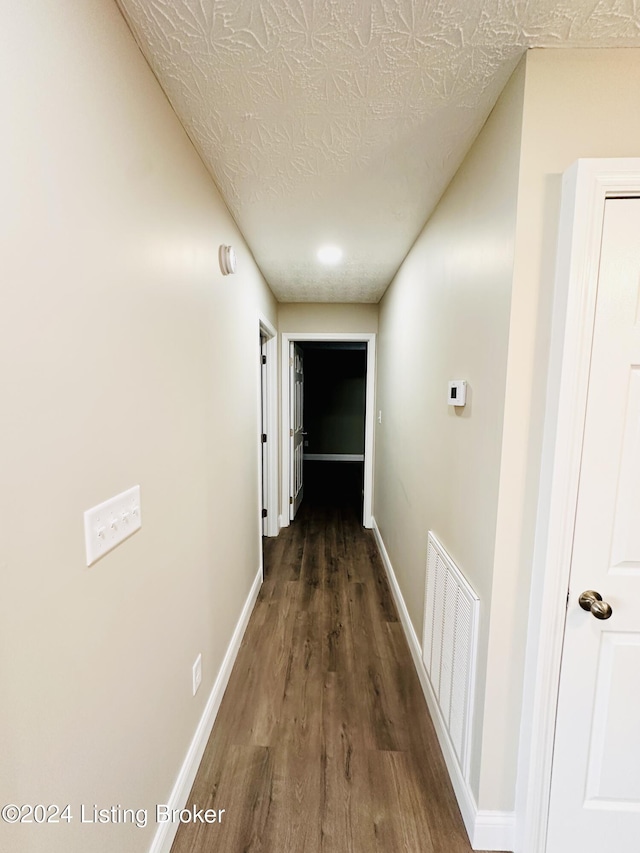 corridor with a textured ceiling and dark hardwood / wood-style floors