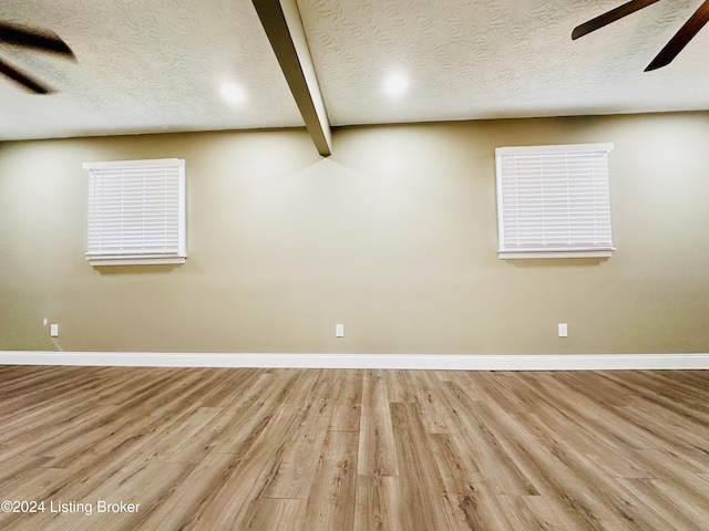 spare room featuring beam ceiling, light hardwood / wood-style flooring, and a textured ceiling