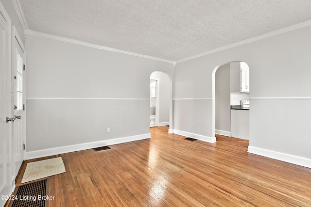 empty room with wood-type flooring, a textured ceiling, and crown molding