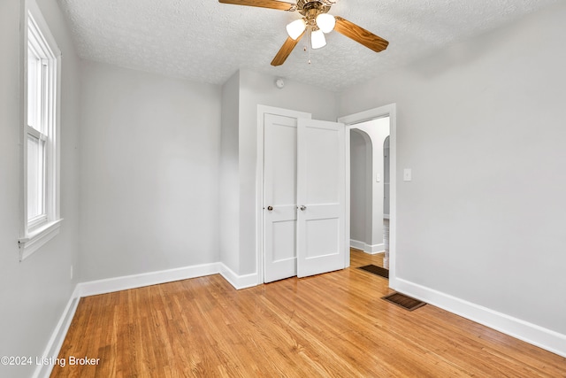 unfurnished bedroom with ceiling fan, a closet, light hardwood / wood-style floors, and a textured ceiling