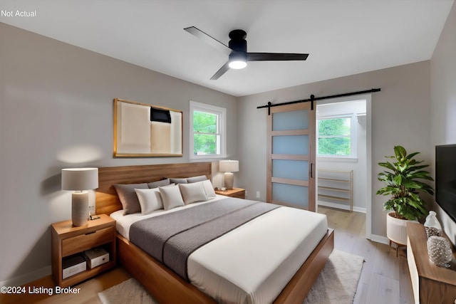 bedroom with ceiling fan, a barn door, and light hardwood / wood-style flooring