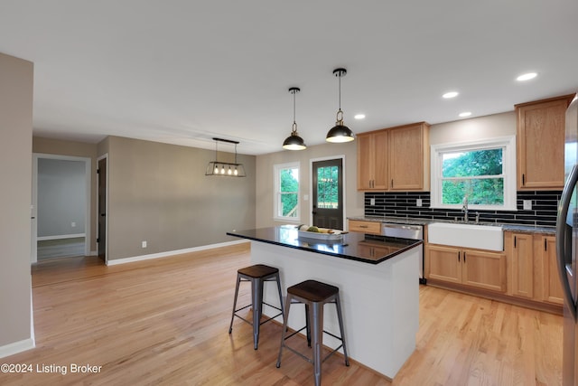 kitchen featuring decorative light fixtures, tasteful backsplash, sink, a center island, and light hardwood / wood-style flooring