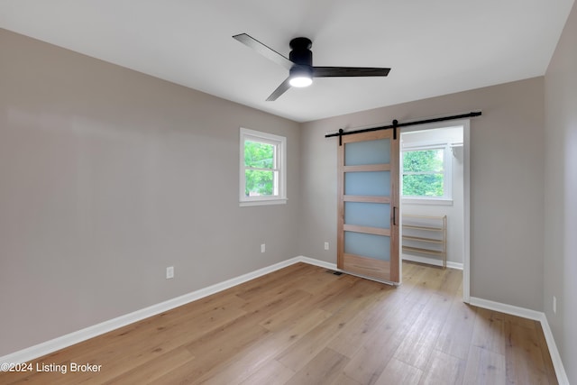 empty room featuring a barn door, ceiling fan, and light hardwood / wood-style flooring