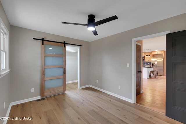 unfurnished bedroom with a barn door, ceiling fan, stainless steel fridge, and light wood-type flooring