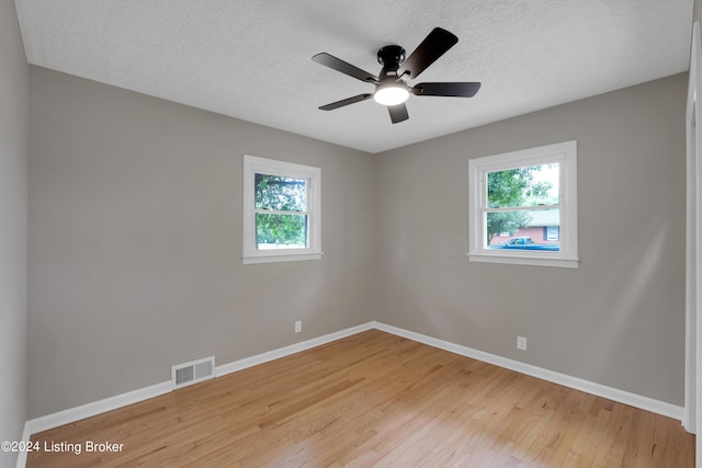 empty room with ceiling fan, plenty of natural light, a textured ceiling, and light wood-type flooring