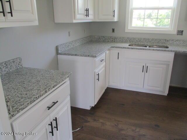 kitchen with light stone countertops, white cabinetry, sink, and dark wood-type flooring