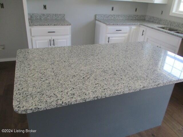 kitchen featuring light stone countertops, dark hardwood / wood-style floors, white cabinetry, and sink