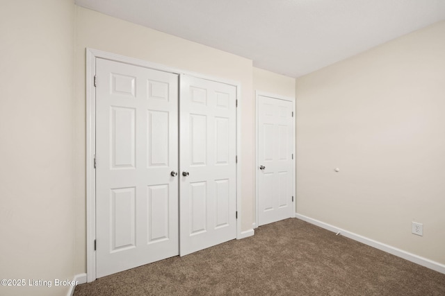 unfurnished bedroom with a closet, baseboards, and dark carpet