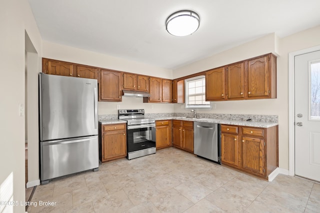 kitchen with under cabinet range hood, appliances with stainless steel finishes, light countertops, and a sink