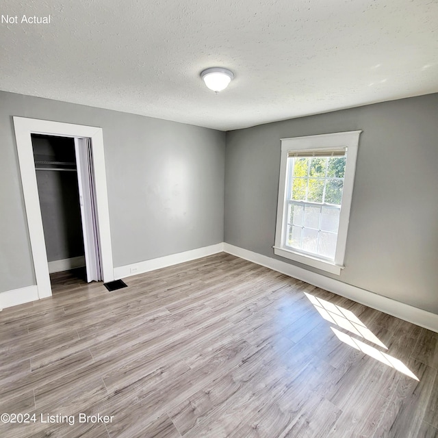 unfurnished bedroom featuring a textured ceiling, light hardwood / wood-style flooring, and a closet