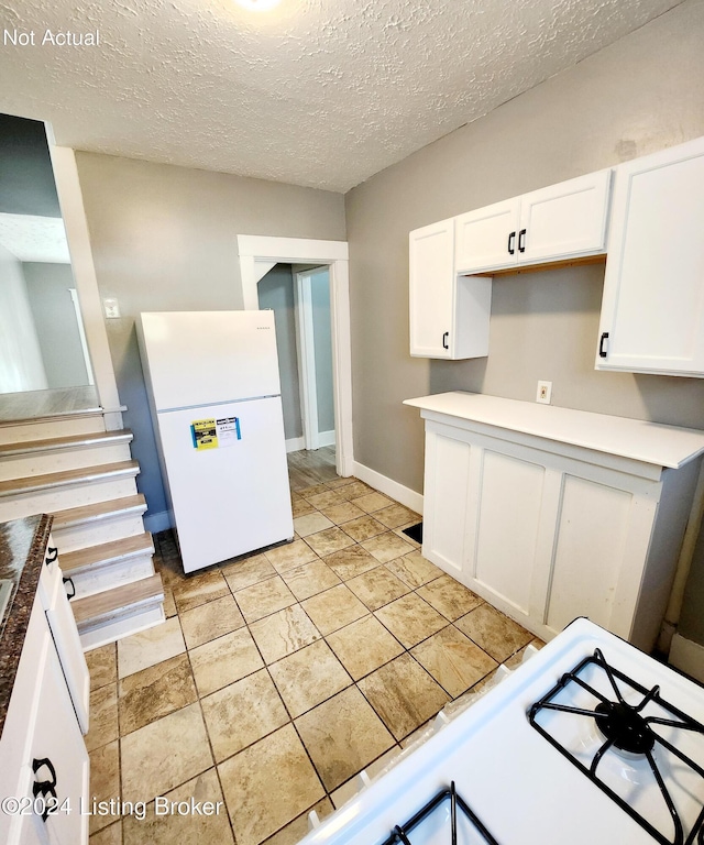 kitchen with white fridge, white cabinetry, and a textured ceiling