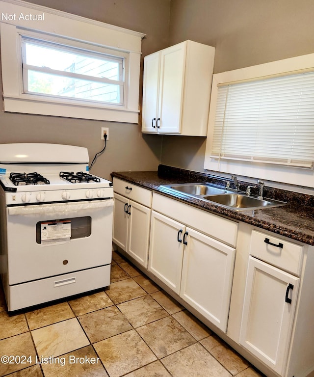 kitchen with sink, light tile patterned floors, dark stone counters, white range with gas cooktop, and white cabinets