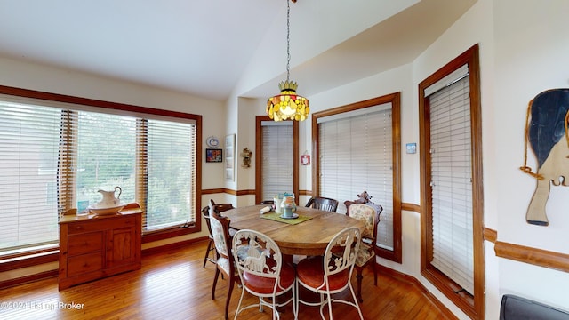 dining area with hardwood / wood-style floors, a chandelier, a healthy amount of sunlight, and vaulted ceiling