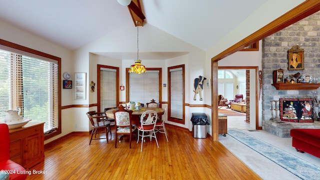 dining room featuring lofted ceiling with beams, light wood-type flooring, a fireplace, and an inviting chandelier