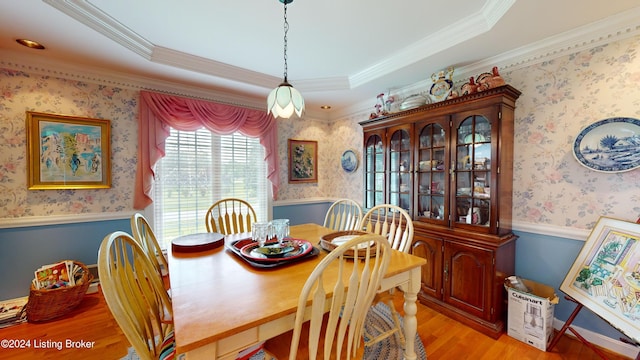 dining room with ornamental molding, a tray ceiling, and light hardwood / wood-style flooring