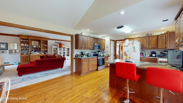 kitchen featuring a kitchen bar, lofted ceiling, appliances with stainless steel finishes, and light hardwood / wood-style flooring