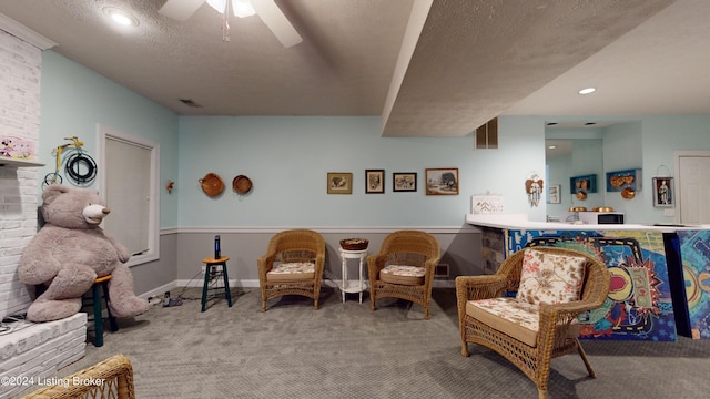 sitting room with ceiling fan, carpet floors, and a textured ceiling