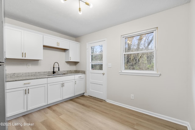 kitchen featuring sink, white cabinetry, light hardwood / wood-style flooring, and light stone countertops