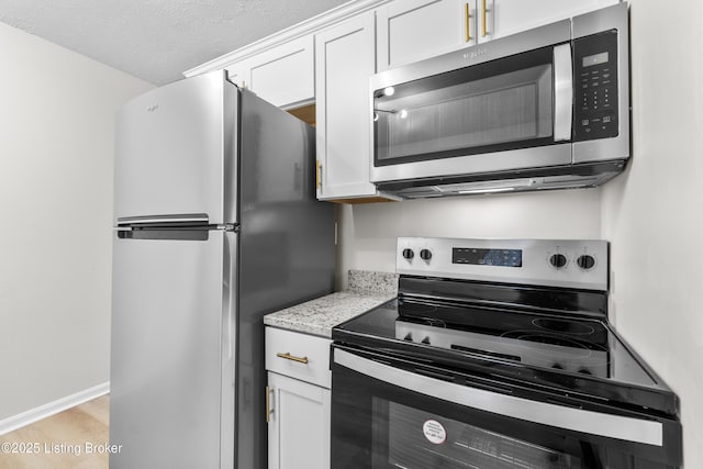 kitchen featuring white cabinetry, a textured ceiling, light stone counters, light hardwood / wood-style flooring, and appliances with stainless steel finishes