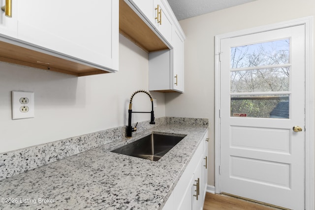 kitchen with sink, light hardwood / wood-style floors, white cabinets, and light stone countertops