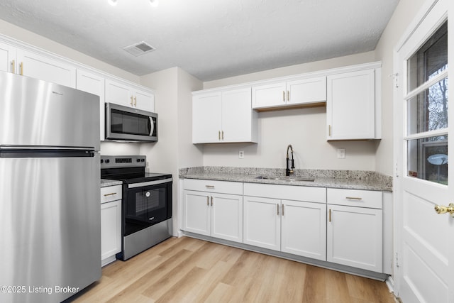 kitchen featuring a textured ceiling, light hardwood / wood-style flooring, stainless steel appliances, white cabinetry, and sink