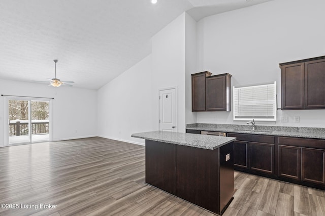 kitchen with sink, dark brown cabinets, light stone countertops, and a center island