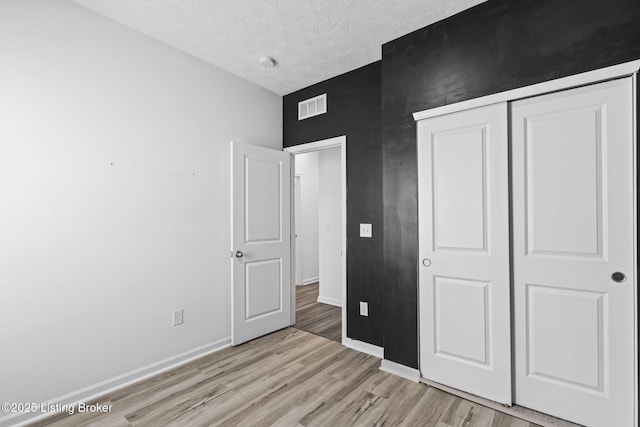 unfurnished bedroom featuring a textured ceiling, a closet, and light hardwood / wood-style flooring