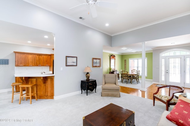 carpeted living room featuring ceiling fan, ornamental molding, and decorative columns