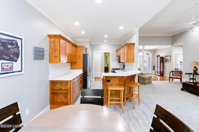 kitchen with kitchen peninsula, backsplash, ceiling fan, crown molding, and stainless steel refrigerator