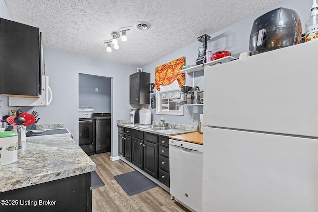 kitchen with sink, light hardwood / wood-style floors, a textured ceiling, white appliances, and washer and clothes dryer