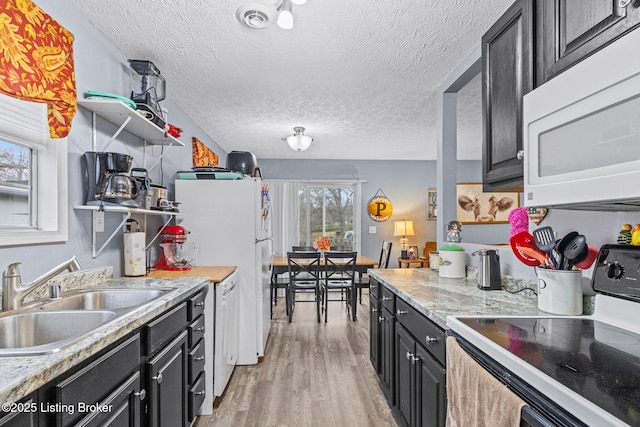 kitchen featuring light stone countertops, a textured ceiling, white appliances, sink, and light hardwood / wood-style floors