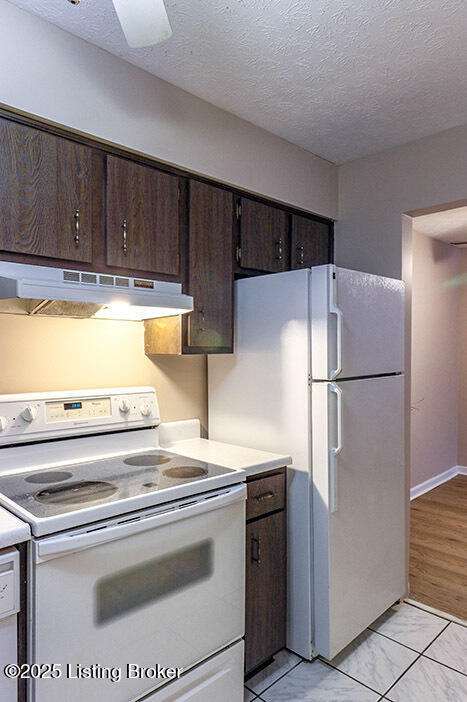 kitchen with dark brown cabinetry, a textured ceiling, and white appliances