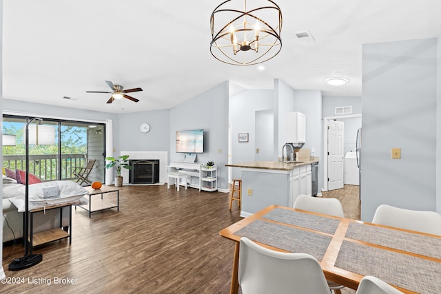 dining room with sink, dark hardwood / wood-style flooring, lofted ceiling, a tiled fireplace, and ceiling fan with notable chandelier