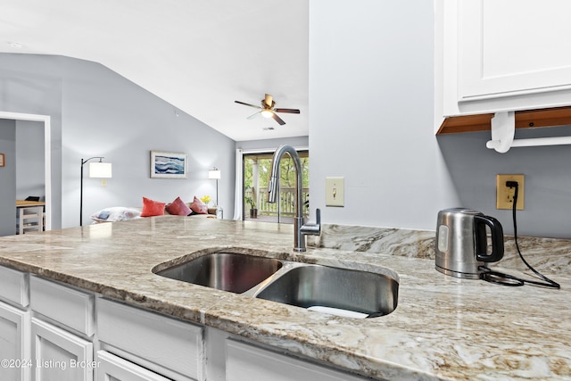 kitchen with white cabinetry, sink, light stone counters, and lofted ceiling