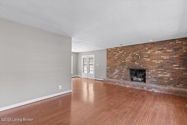 unfurnished living room with hardwood / wood-style floors, a textured ceiling, and a brick fireplace