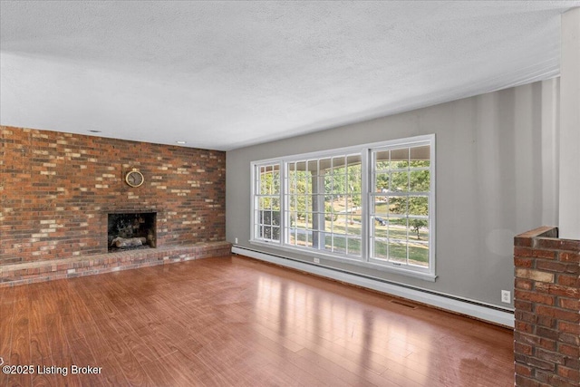 unfurnished living room featuring hardwood / wood-style flooring, a fireplace, a textured ceiling, and a baseboard heating unit