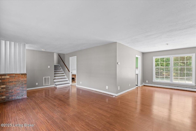 unfurnished living room featuring wood-type flooring, a textured ceiling, and baseboard heating