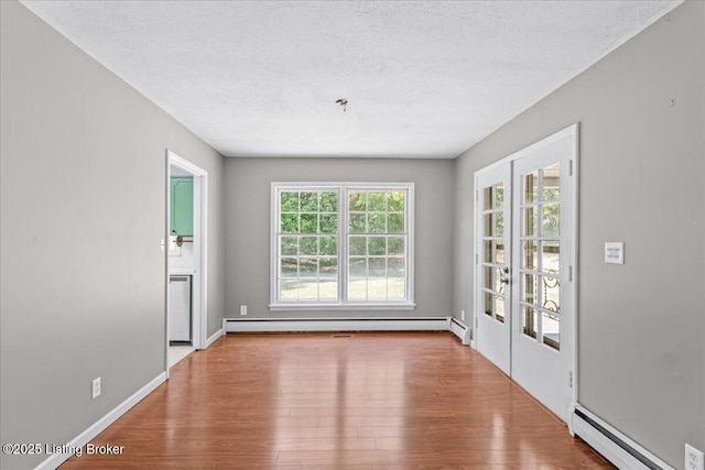 empty room featuring hardwood / wood-style floors, a textured ceiling, and baseboard heating