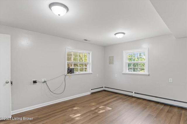 empty room with hardwood / wood-style flooring, a baseboard radiator, and a healthy amount of sunlight