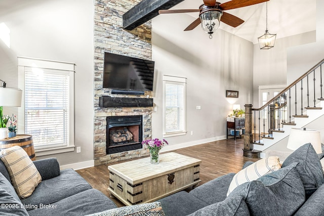 living room with a towering ceiling, ceiling fan, dark wood-type flooring, beam ceiling, and a fireplace