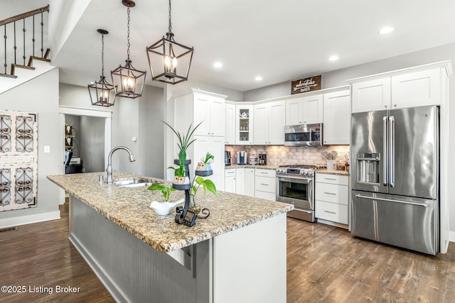 kitchen with a kitchen island with sink, white cabinets, sink, appliances with stainless steel finishes, and decorative light fixtures