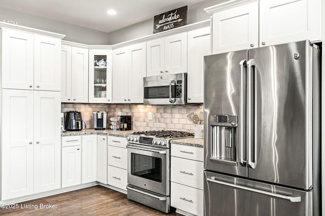 kitchen featuring white cabinets, appliances with stainless steel finishes, light stone counters, and dark wood-type flooring