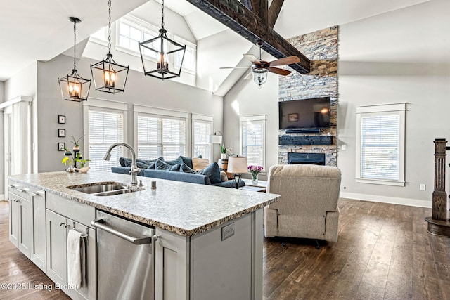 kitchen featuring beam ceiling, sink, a stone fireplace, an island with sink, and decorative light fixtures