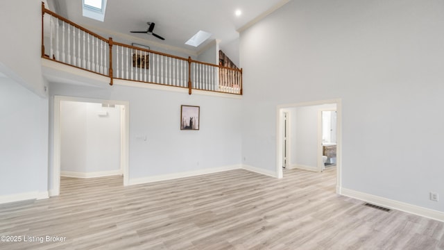 unfurnished living room featuring a towering ceiling, light hardwood / wood-style flooring, ceiling fan, and a skylight