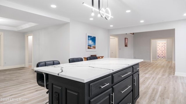 kitchen featuring a kitchen bar, light hardwood / wood-style flooring, a kitchen island, pendant lighting, and light stone countertops