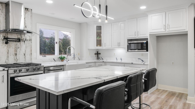 kitchen featuring stainless steel appliances, light stone counters, white cabinets, a kitchen island, and wall chimney exhaust hood