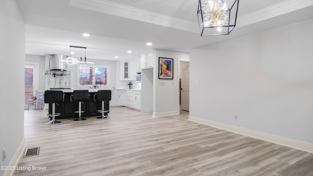 dining area with crown molding, light hardwood / wood-style floors, a raised ceiling, and bar area