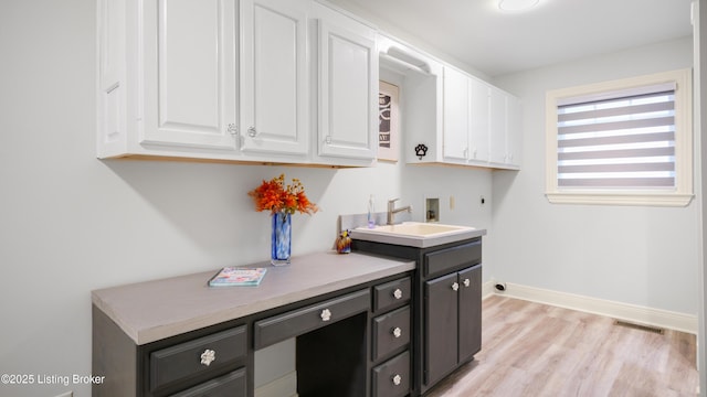 laundry room featuring sink, electric dryer hookup, hookup for a washing machine, cabinets, and light hardwood / wood-style floors