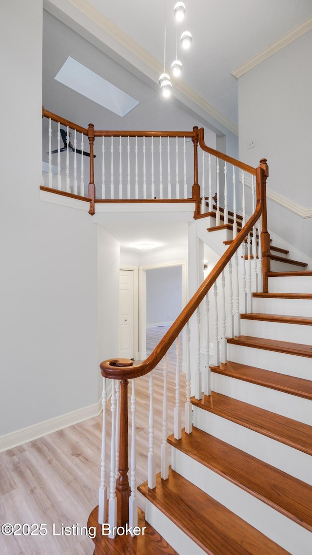 staircase with crown molding, wood-type flooring, and a skylight